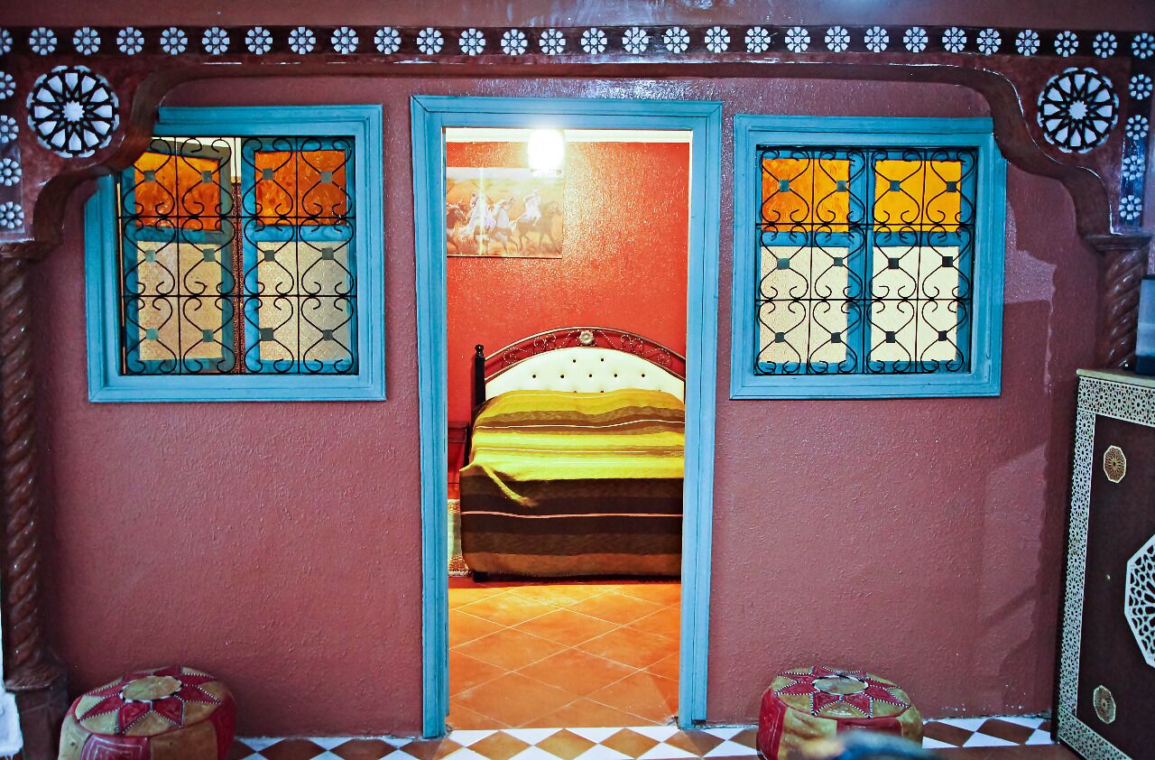 Ein Zimmer mit einem Bett, zwei Fenstern mit blauen Rahmen und einer Wand mit Muster.