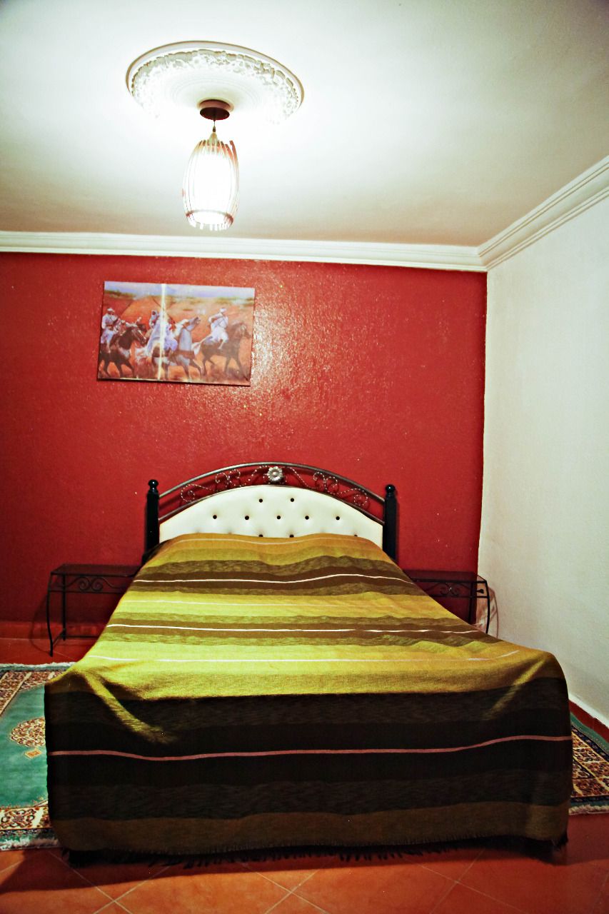 Una cama en una habitación con una pared roja y un cuadro encima.