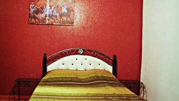 Una cama en una habitación con una pared roja y un cuadro encima.