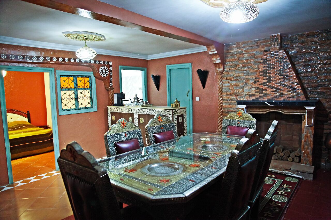 A dining area with a glass table, patterned chairs, and a brick wall with a fireplace.