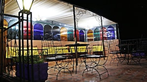 An outdoor seating area with metal chairs and tables, a decorative lamp, and a row of colorful glass doors.