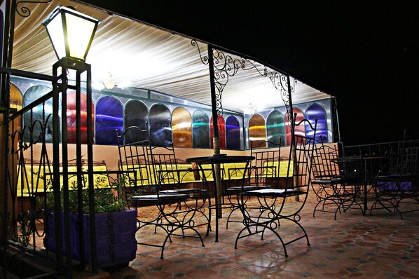 An outdoor seating area with metal chairs and tables, a decorative lamp, and a row of colorful glass doors. - Naima House (Taroudant)