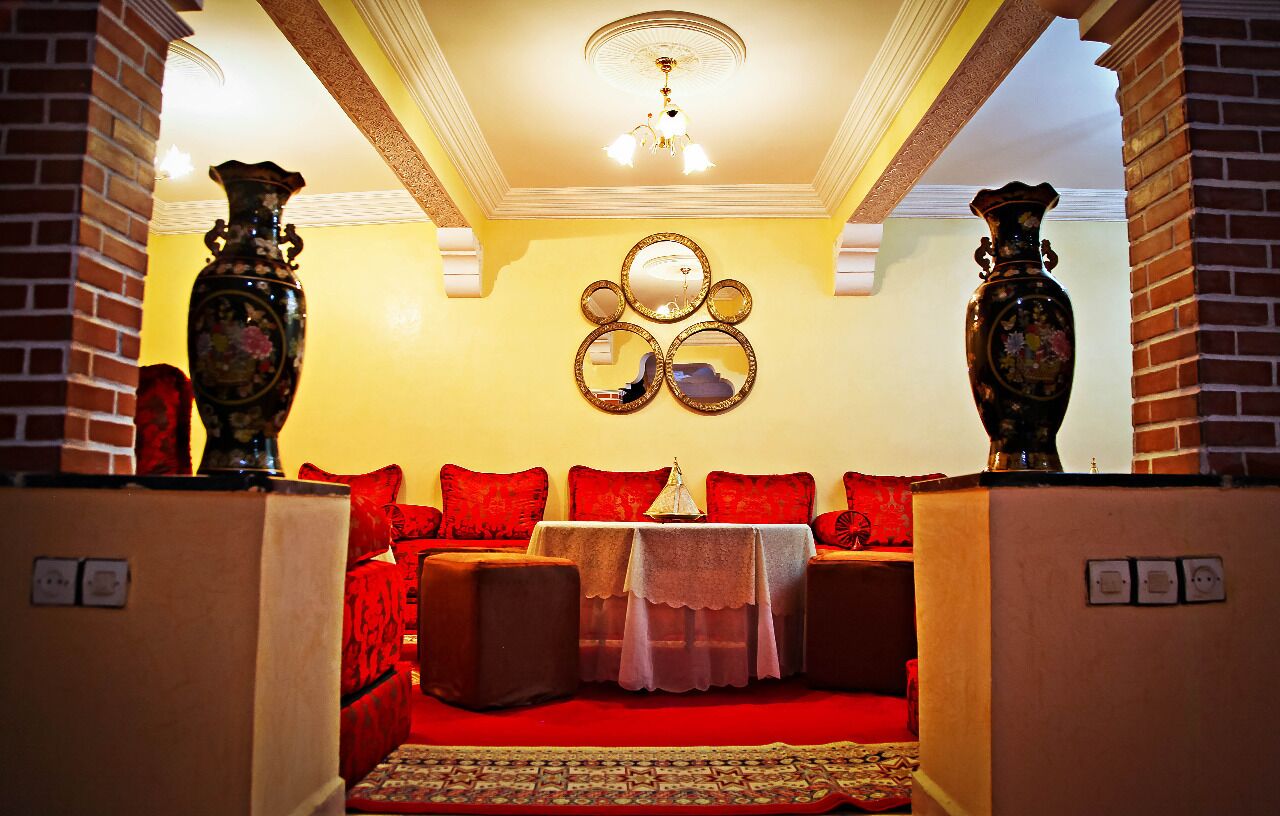 A cozy room with a red sofa set, a small table with a lace tablecloth, and two large vases on either side.