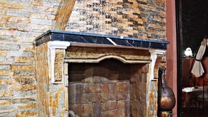 A fireplace with a stone wall, a log storage area, and a patterned rug.