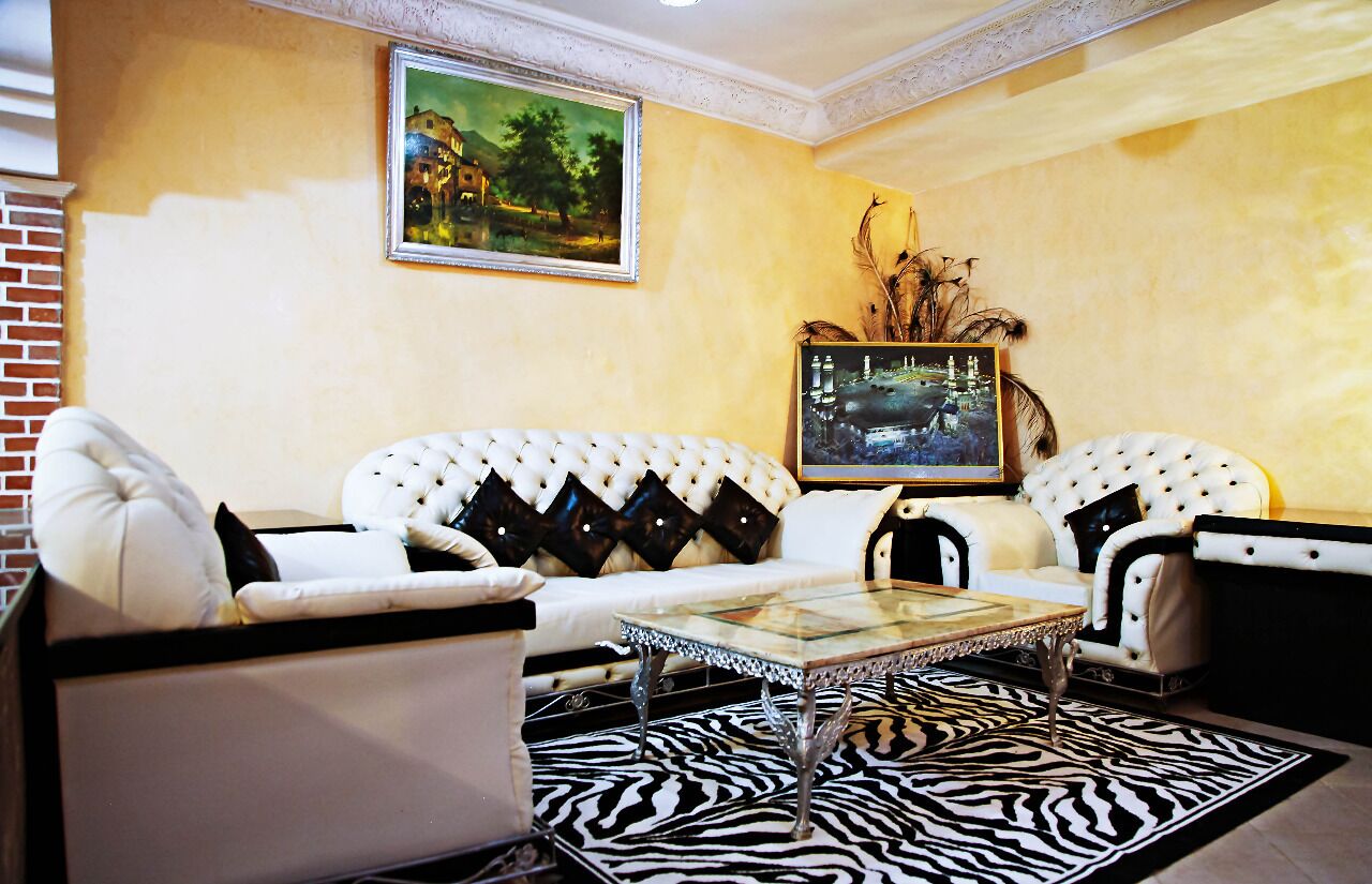 Una sala de estar con un sofá blanco, dos sillones, una mesa de centro de vidrio y un tapete con estampado de cebra.