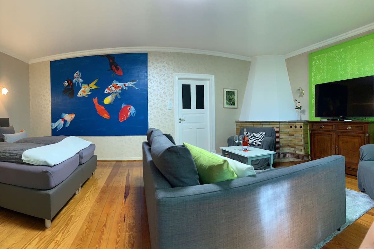 A modern bedroom with a large bed, a sofa, a TV, and a mural of fish on the wall.