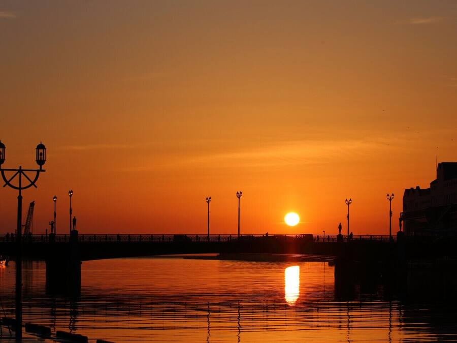 Un atardecer sobre un muelle con un puente, farolas y una estatua.