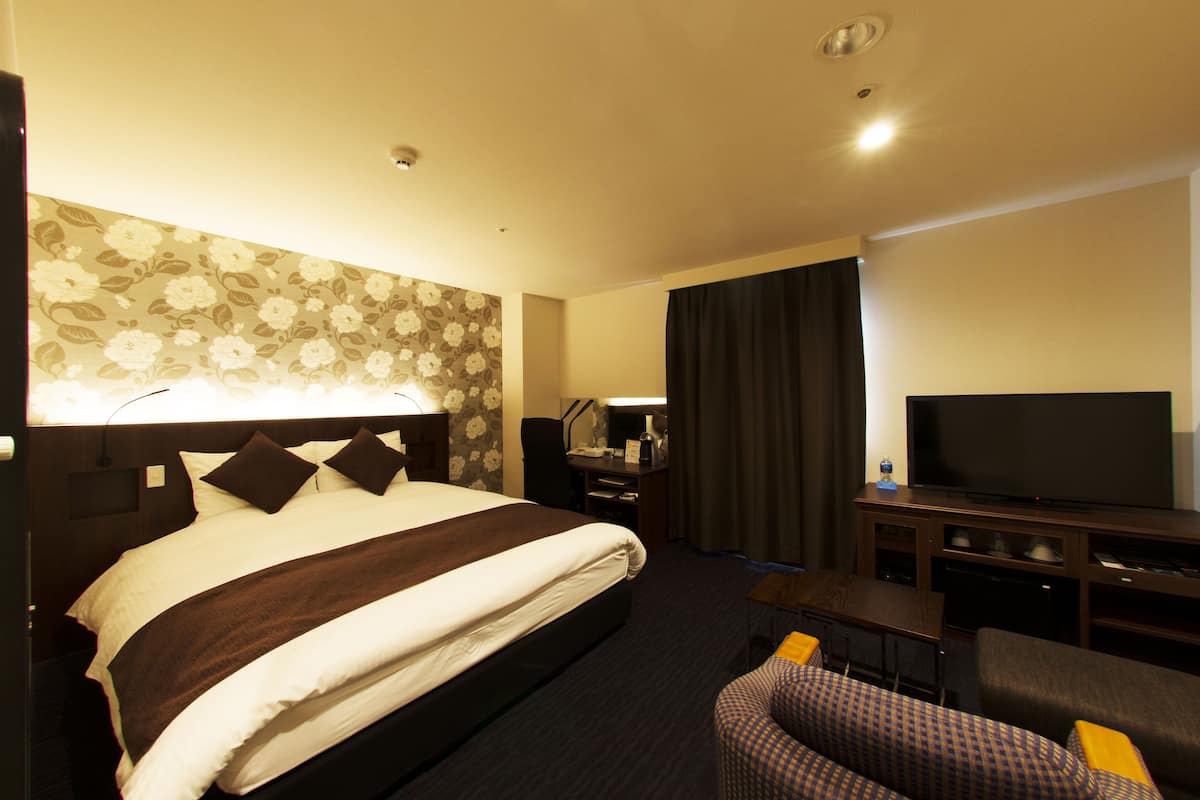 A hotel room with a large bed, a desk with a computer, a television, and a seating area with a chair.