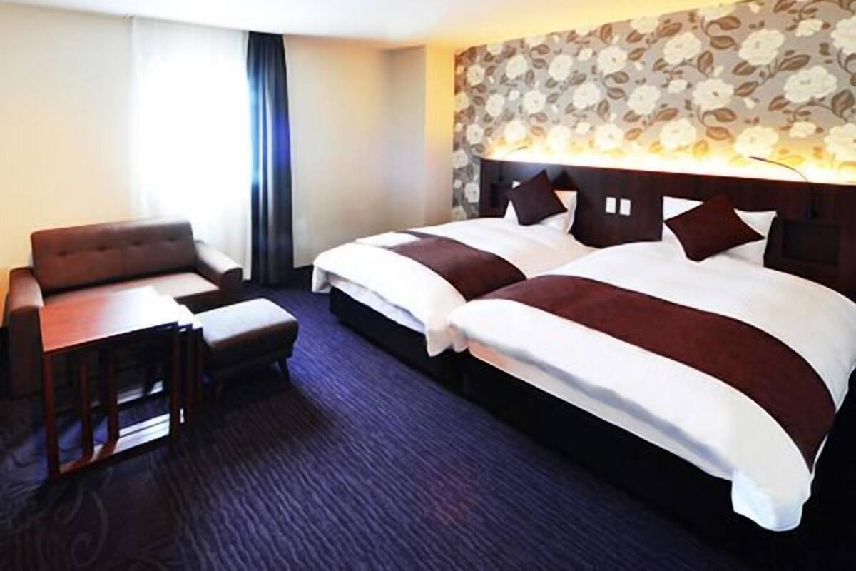 A hotel room with a bed, a desk, a chair, and a window with curtains.