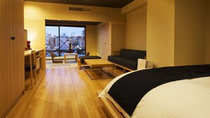 A modern hotel room with a large bed, a sofa, a dining table, and a view of the cityscape through a large window. - Kushiro Century Castle Hotel (Kushiro)