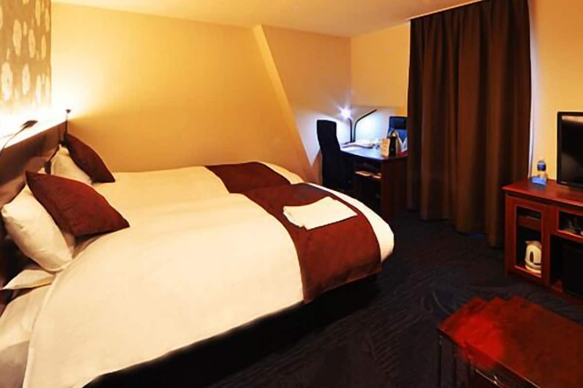 A hotel room with a bed, desk, chair, television, and curtains.