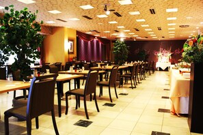 A spacious dining area with multiple tables and chairs, a stage with curtains, and potted plants. - Kushiro Century Castle Hotel (Kushiro)
