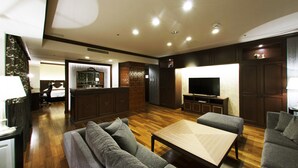 A modern living room with a sofa, a coffee table, and a TV. There is a kitchen area in the background. - Kushiro Century Castle Hotel (Kushiro)