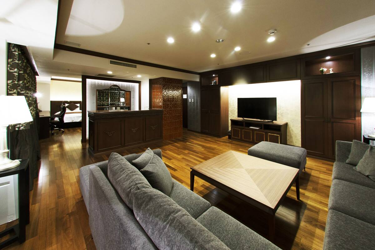 A modern living room with a sofa, a coffee table, and a TV. There is a kitchen area in the background.