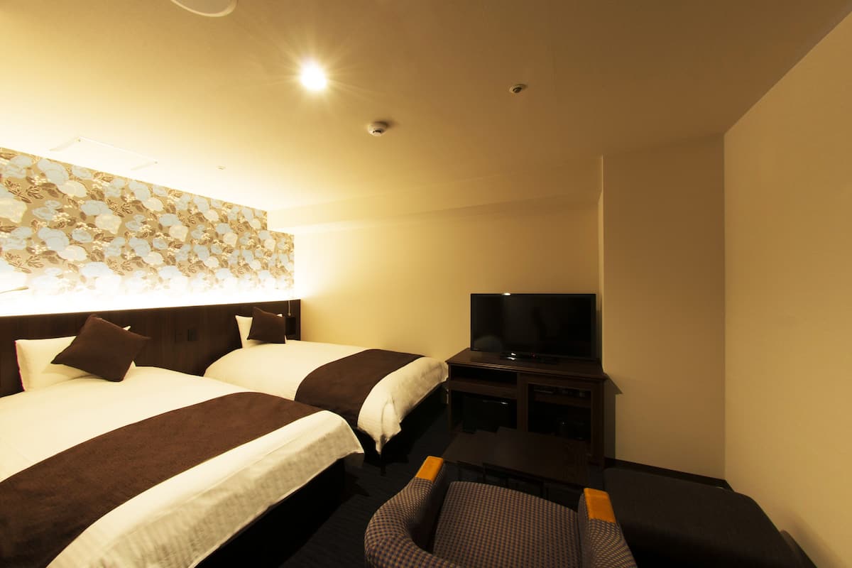 A hotel room with two beds, a TV, and a desk.