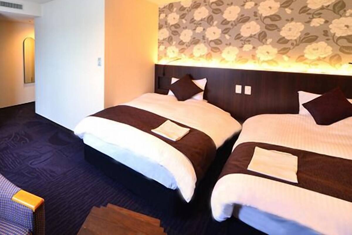 A hotel room with two beds, a floral-patterned headboard, and a dark carpet.
