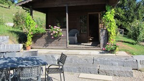 Una cabaña de madera con porche, escalones de piedra y mobiliario exterior.