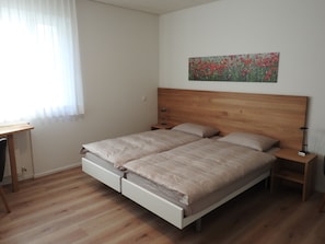Un dormitorio con cabecera de madera, dos camas, un escritorio y una mesita de noche.
