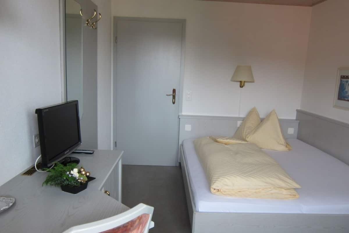 A hotel room with a bed, a desk with a computer monitor, a lamp, and a door.
