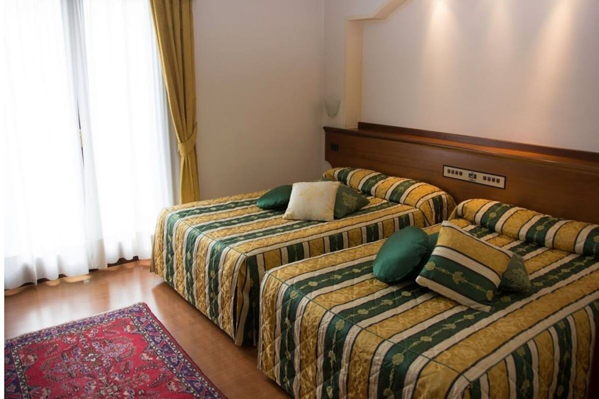 A hotel room with two beds, a red patterned rug, and a wooden headboard.