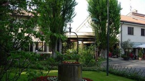 A garden with a central fountain, surrounded by a circular flower bed with red and white flowers. - Hotel Piroga Padova (Selvazzano Dentro)