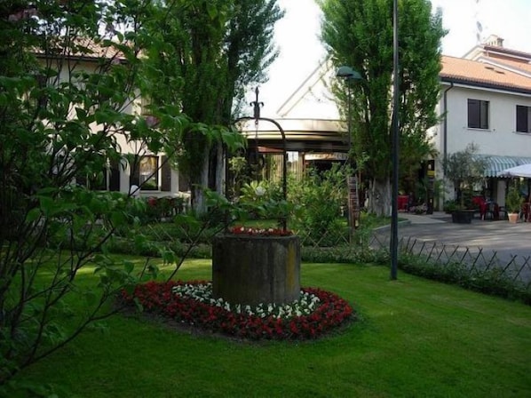 A garden with a central fountain, surrounded by a circular flower bed with red and white flowers. - Hotel Piroga Padova (Selvazzano Dentro)