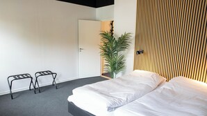 A bedroom with a bed, two black metal stools, a potted plant, and a wooden slatted wall. - Stay and Sleep (Grindsted)