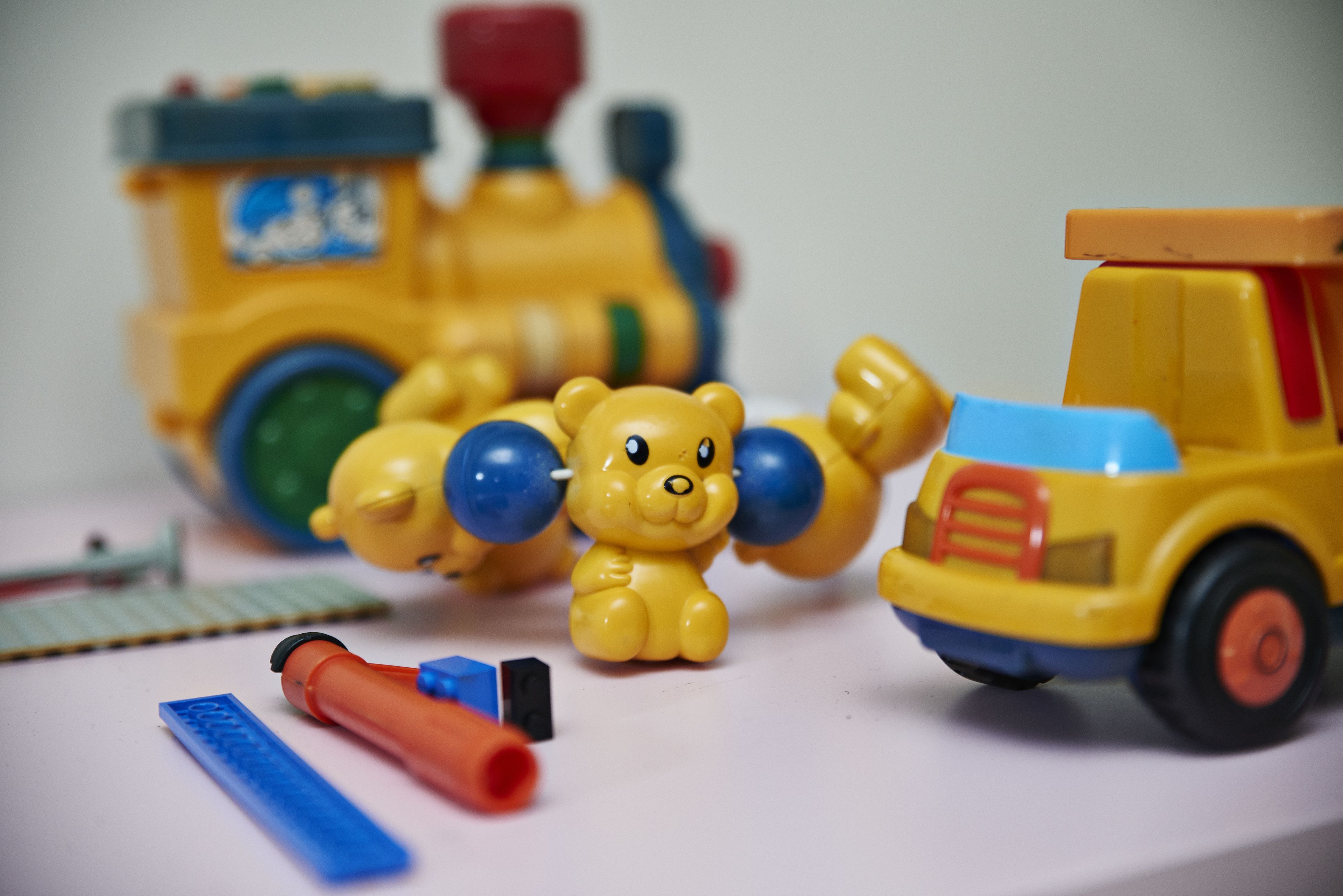 A toy train, a toy truck, and a toy bear on a table.