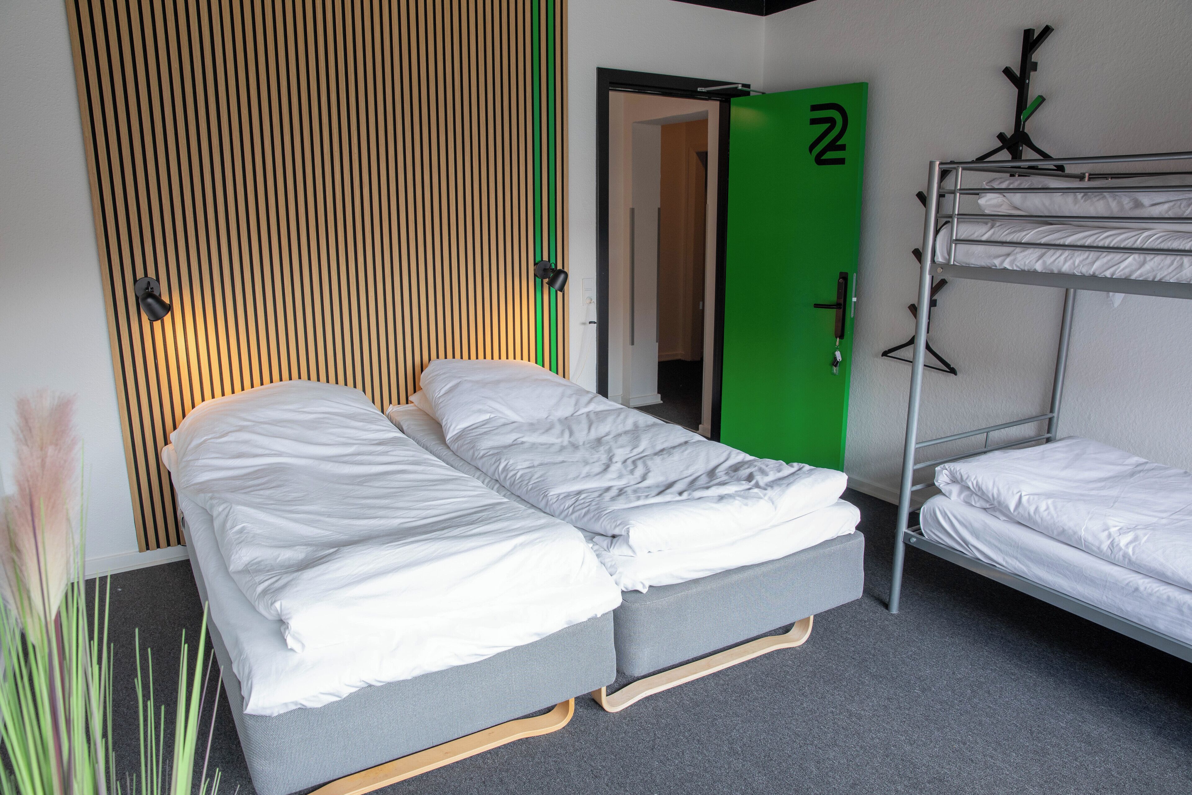 A room with two single beds, a bunk bed, a green door, and a vertical wooden slat wall.
