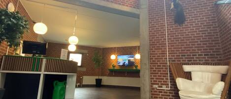 Tilava aula, jossa on korkea katto, kyltti, jossa lukee ”Majoittuminen ja yöpyminen”, vastaanottotiski, televisio ja oleskelualue.