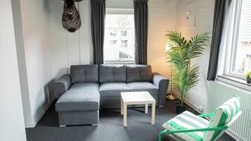 Una sala moderna con un sofá seccional gris, una mesita de madera, una silla verde y blanca a rayas, una planta en maceta y una cabeza de animal montada.