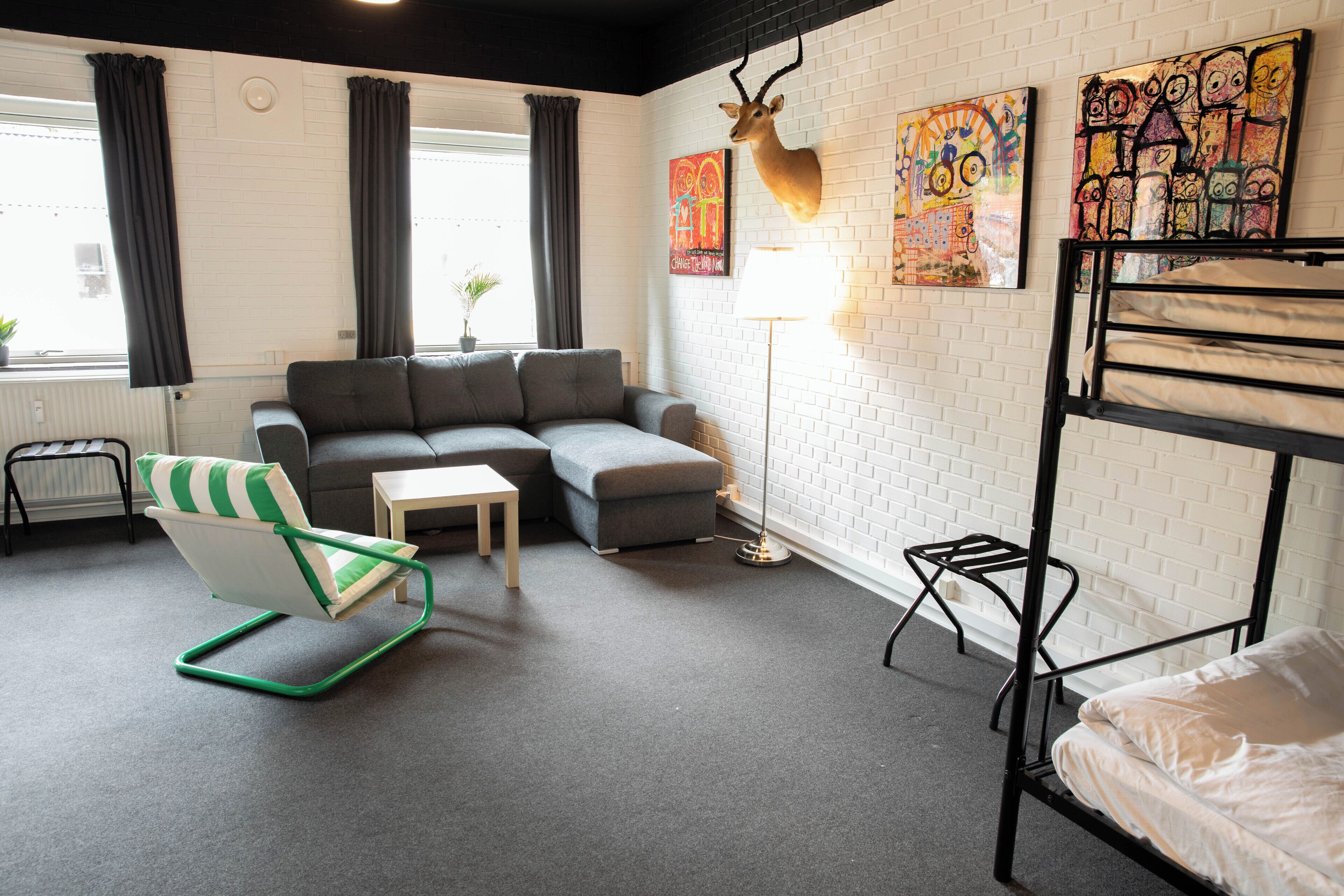 A room with a sofa, a chair, a lamp, a bed, and artwork on the wall.