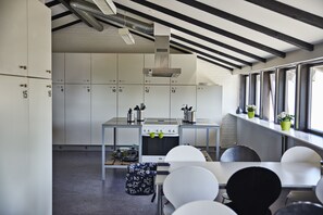 A modern kitchen with white cabinets, a stove, and a dining area with white chairs. - Stay and Sleep (Grindsted)