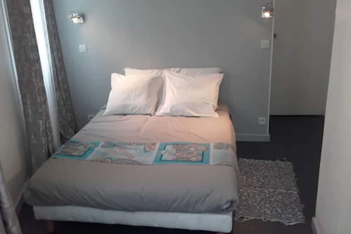 Uma cama com roupa de cama branca, um cobertor estampado e um tapete pequeno.