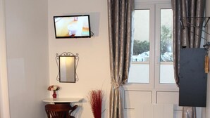 Een slaapkamer met twee bedden, een bureau, een stoel, een televisie en een raam met gordijnen.
