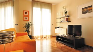 A living room with a sofa, TV, wooden flooring, and a plant.