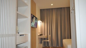 Ein Hotelzimmer mit Bett, Schreibtisch mit Stuhl, einem kleinen Tisch, einem Mülleimer und einem Bild an der Wand.