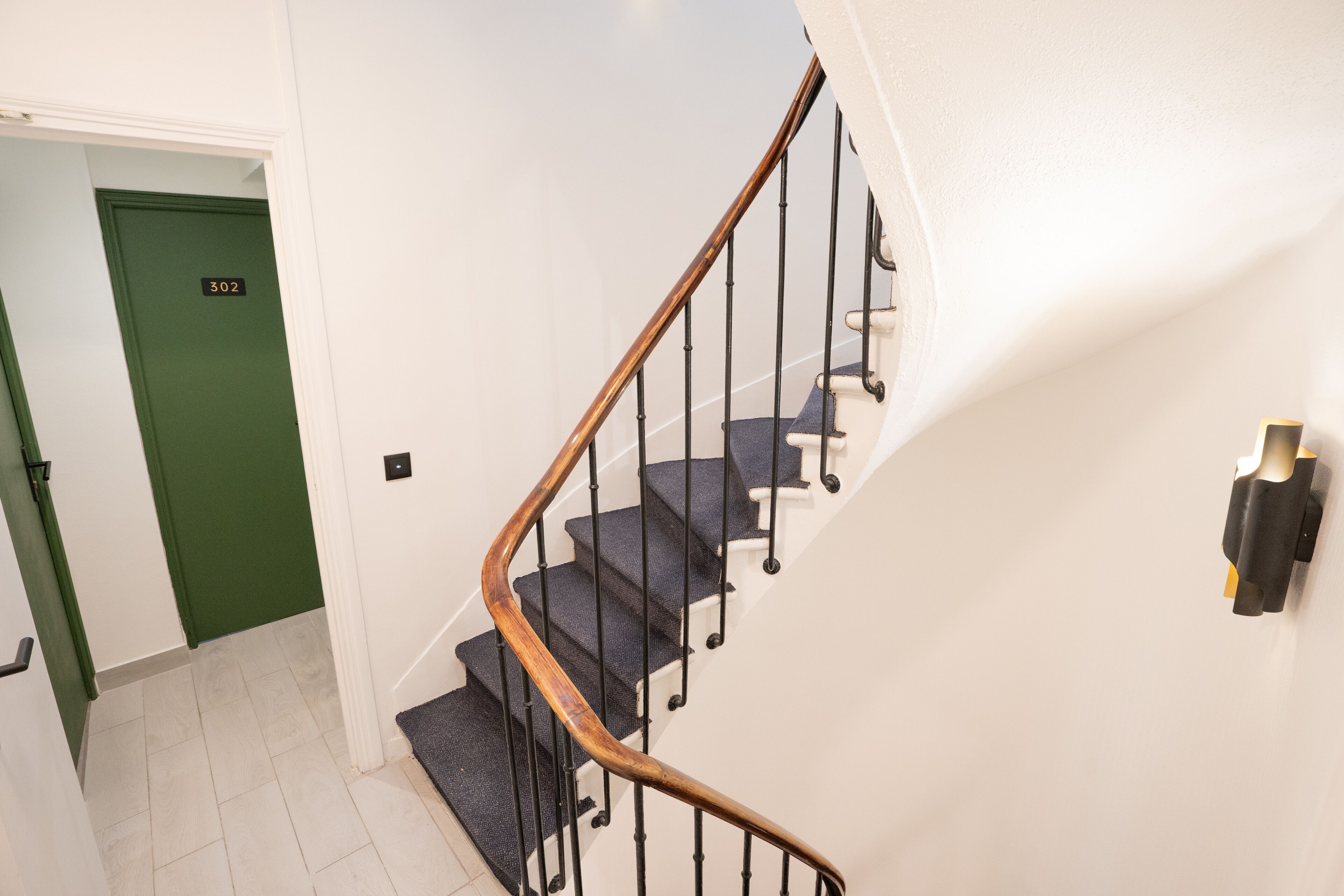 Een trap met een houten leuning en zwarte spijbels, die uitkomt op een plateau met een groene deur waarop 