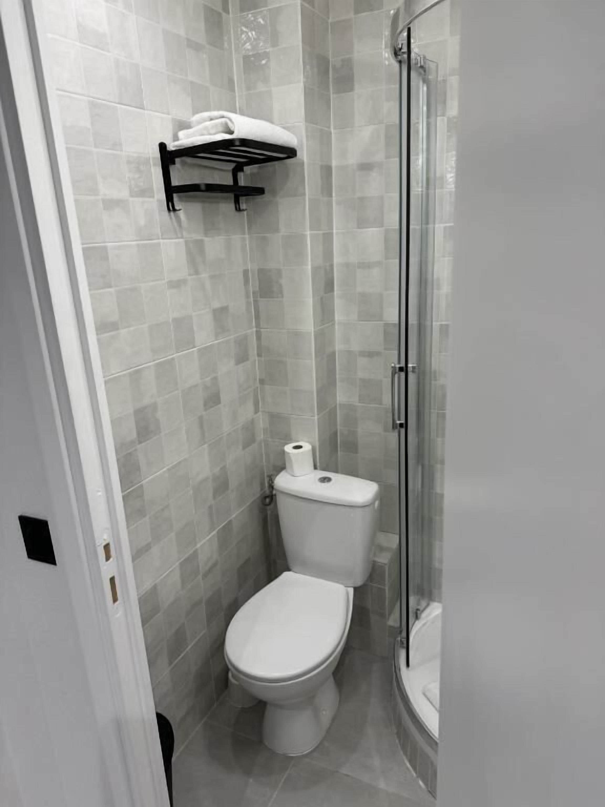 A small, modern bathroom with a toilet, a glass shower enclosure, and a towel rack.