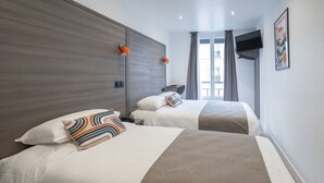 A hotel room with two beds, a flat-screen TV mounted on the wall, and a window with curtains. - Hotel Esperance (Paris)