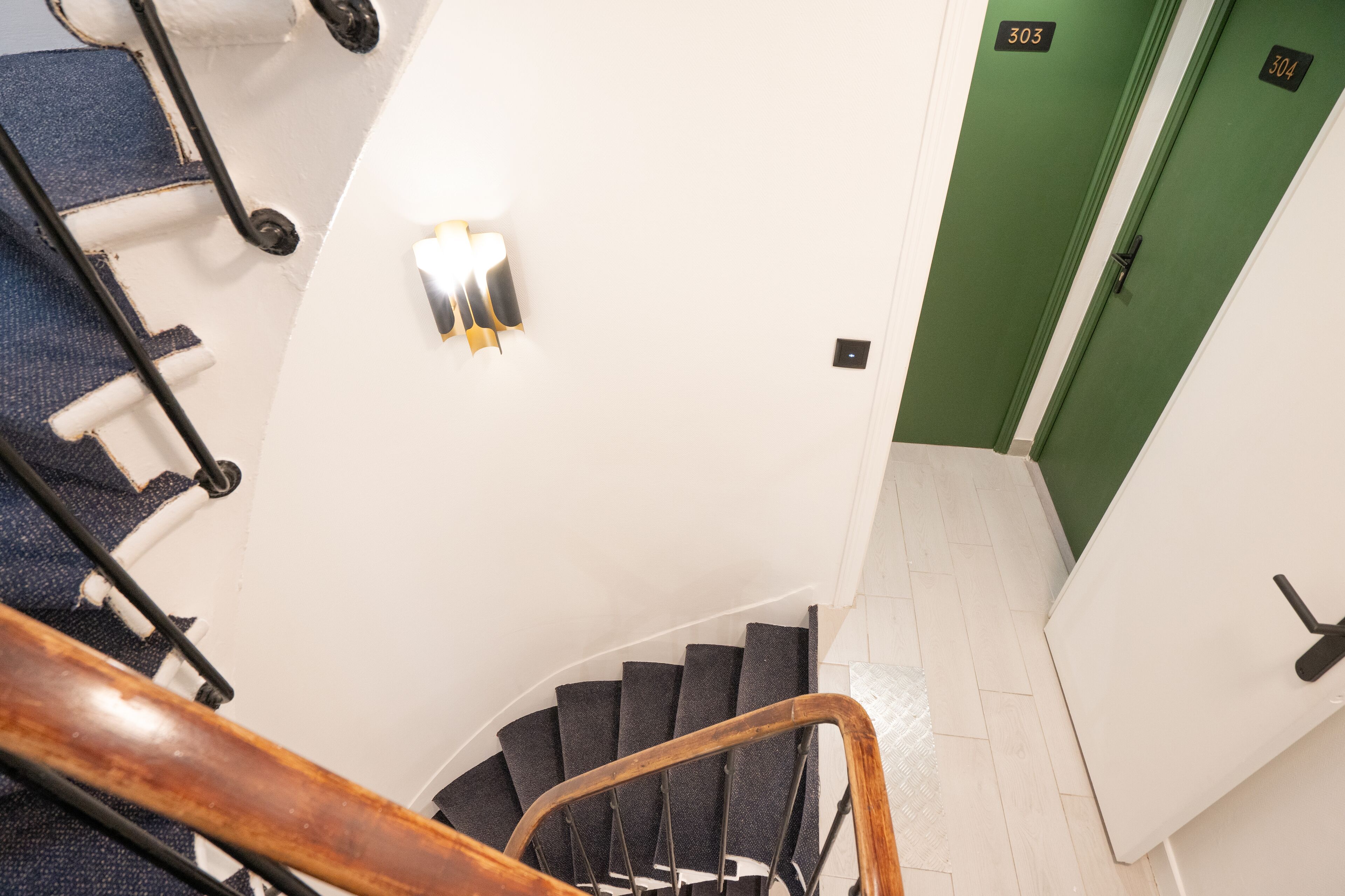 A spiral staircase with a wooden handrail, white walls, and a green door.