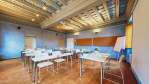Une salle de conférence dotée de parquets en bois, de tables et de chaises blanches, d’un tableau blanc et d’un projecteur fixé au plafond.