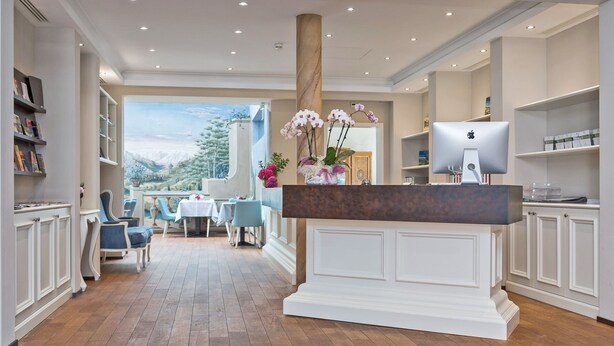 Un hall d’hôtel spacieux, doté d’un comptoir d’accueil en bois, de meubles blancs et offrant une vue sur un paysage montagneux grâce à de grandes fenêtres.