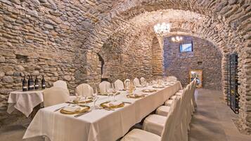 Una larga mesa dispuesta para una cena formal en una sala con paredes de piedra y una araña.