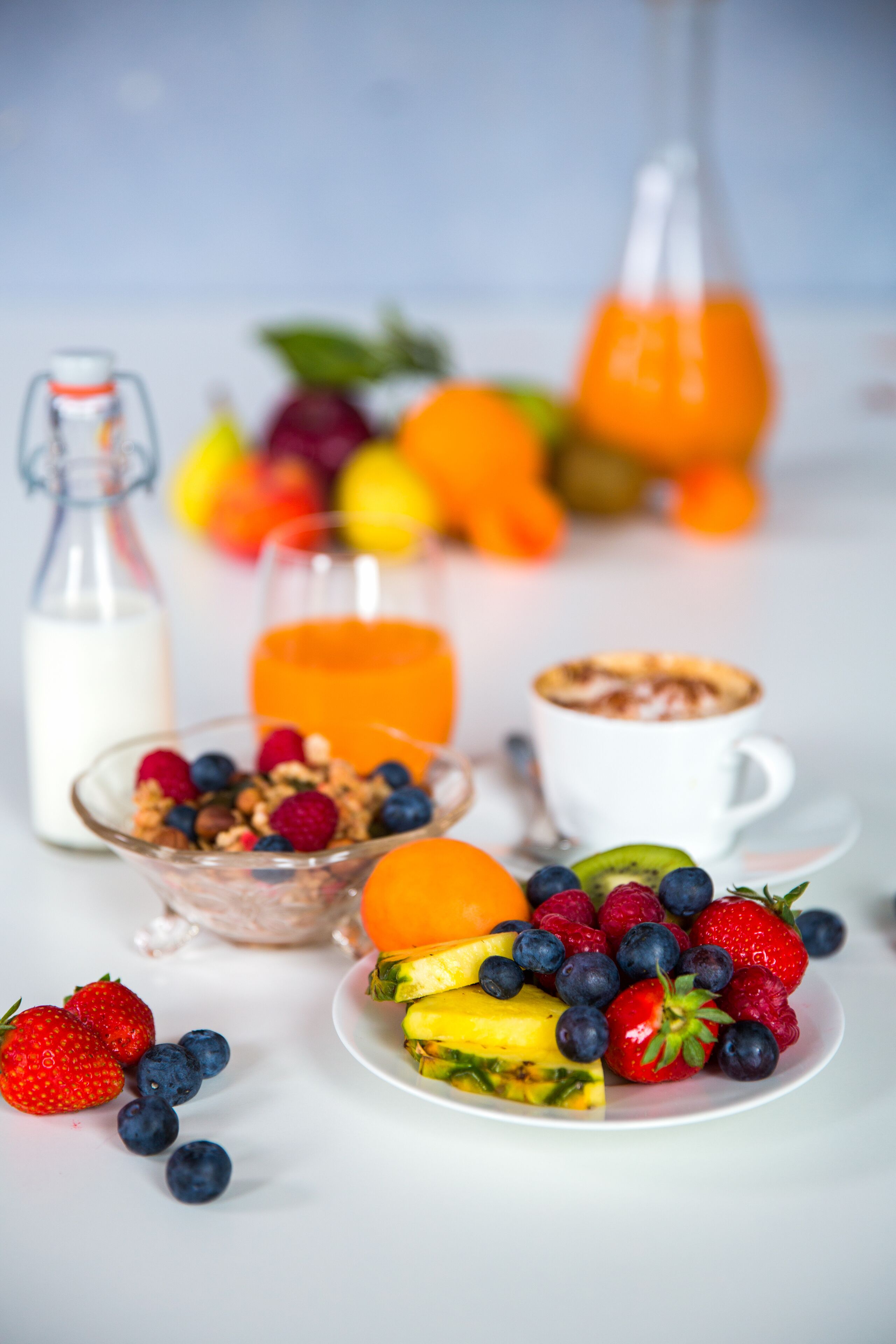 A breakfast setting with various fruits, a glass of orange juice, a bottle of milk, and a cup of coffee.