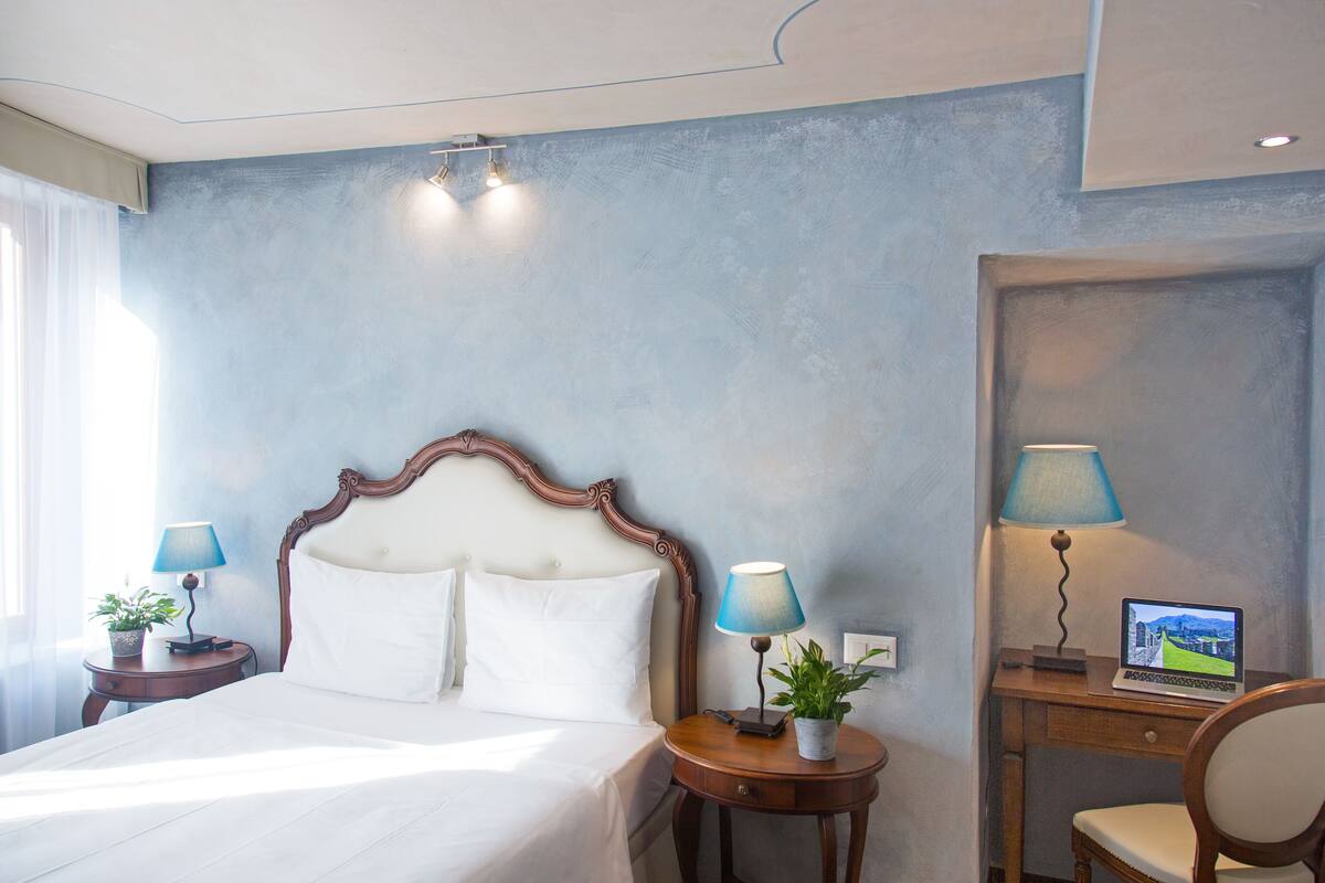Ein Hotelzimmer mit einem Bett, zwei Nachttischen mit Lampen, einem Schreibtisch mit einem Laptop und einem Sessel.