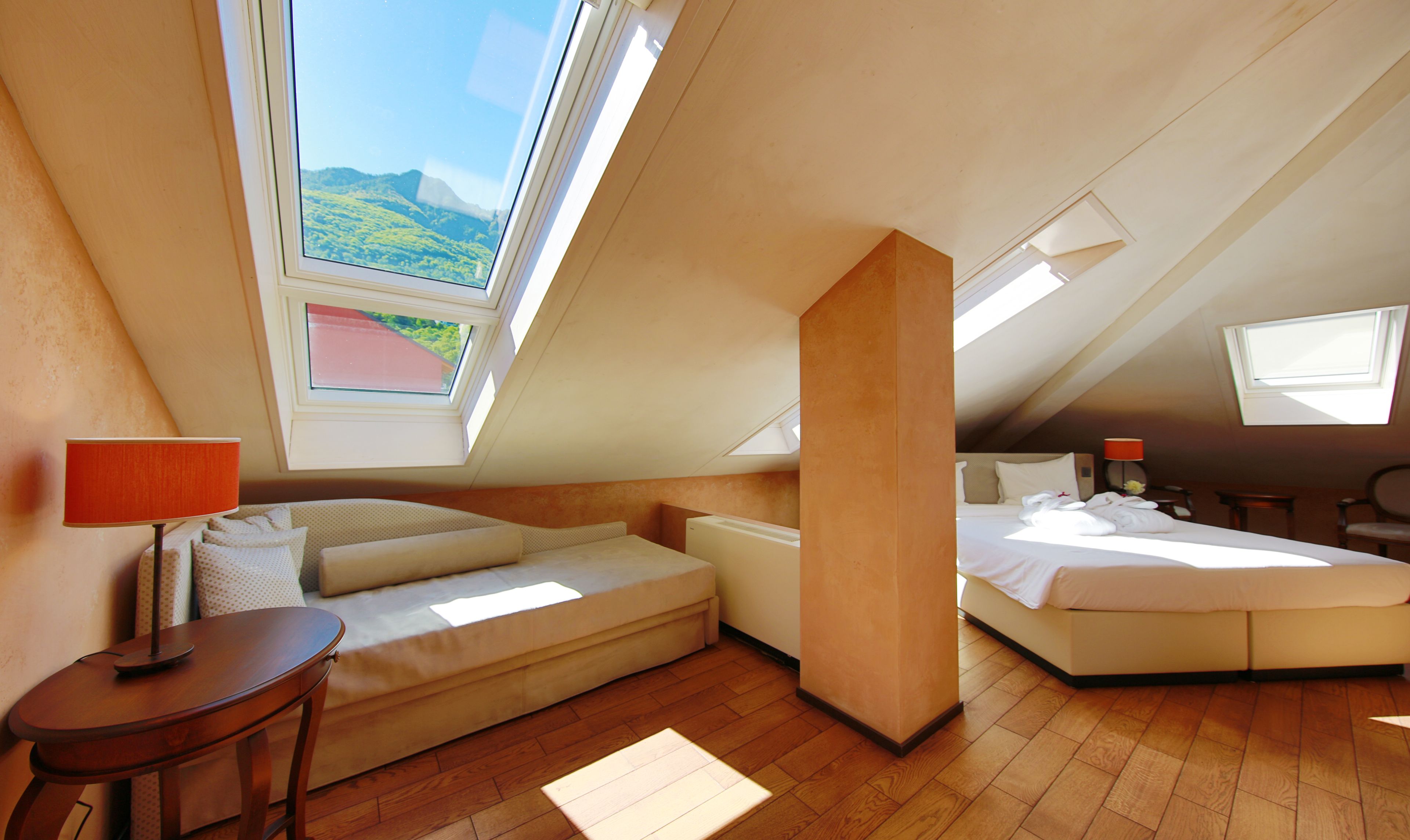 Une chambre confortable située sous les toits, avec une grande fenêtre de toit, un canapé, un lit et une petite table.