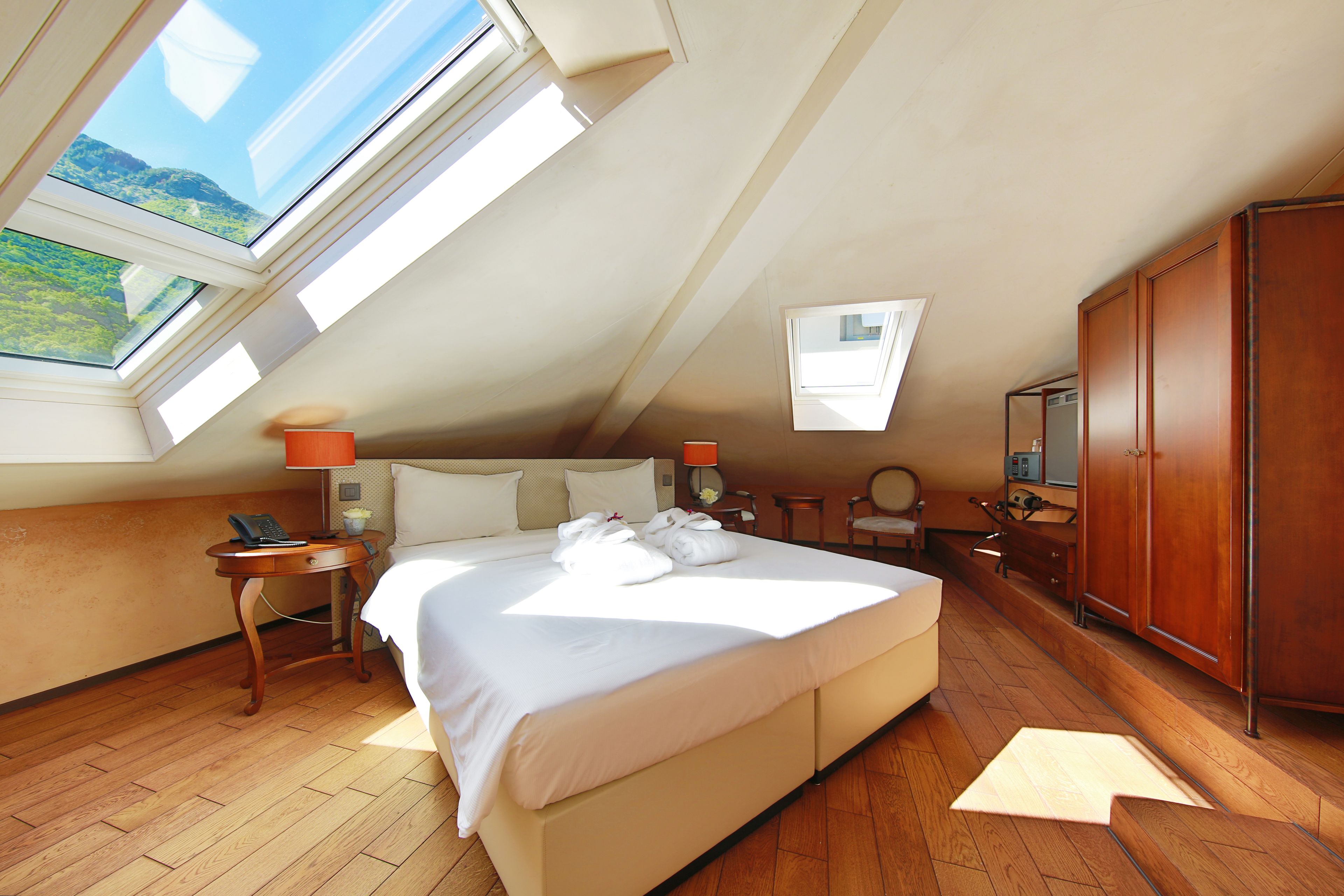 A hotel room with a large bed, a wooden floor, a wardrobe, and a skylight.