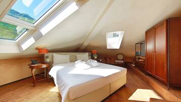 A hotel room with a large bed, a wooden floor, a wardrobe, and a skylight.