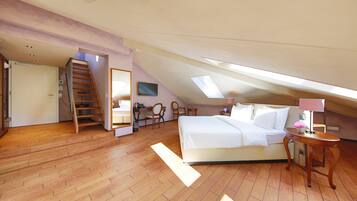 A bedroom with a sloped ceiling, wooden flooring, a bed, a desk, chairs, and a staircase.